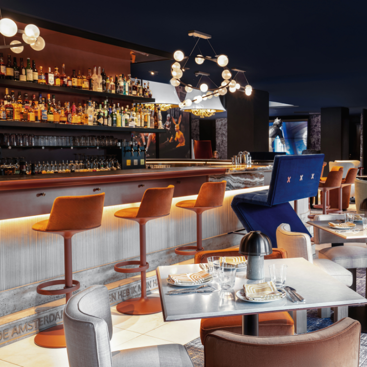 A vibrant bar at Bar Restaurant Prins & Aap featuring orange bar stools and a large bottle display.